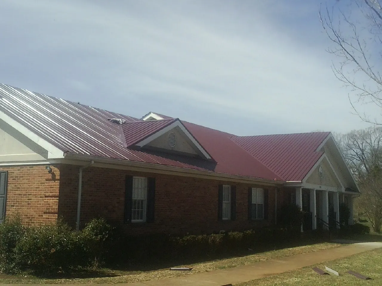 Red metal roof with gabled entries on a long brick building, from a Hail Damage Roof Repair job in Penn