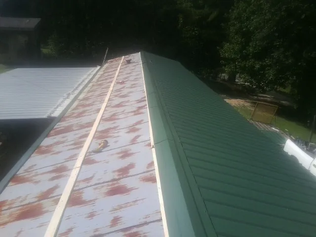 Old rusted panels beside newly installed green metal roofing — Wind Damage Roof Repair by Roofing Brothers in Penn