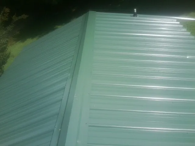 New green metal panels meeting at the ridge of a roof — Flat Roof Repair work by our crew in Penn