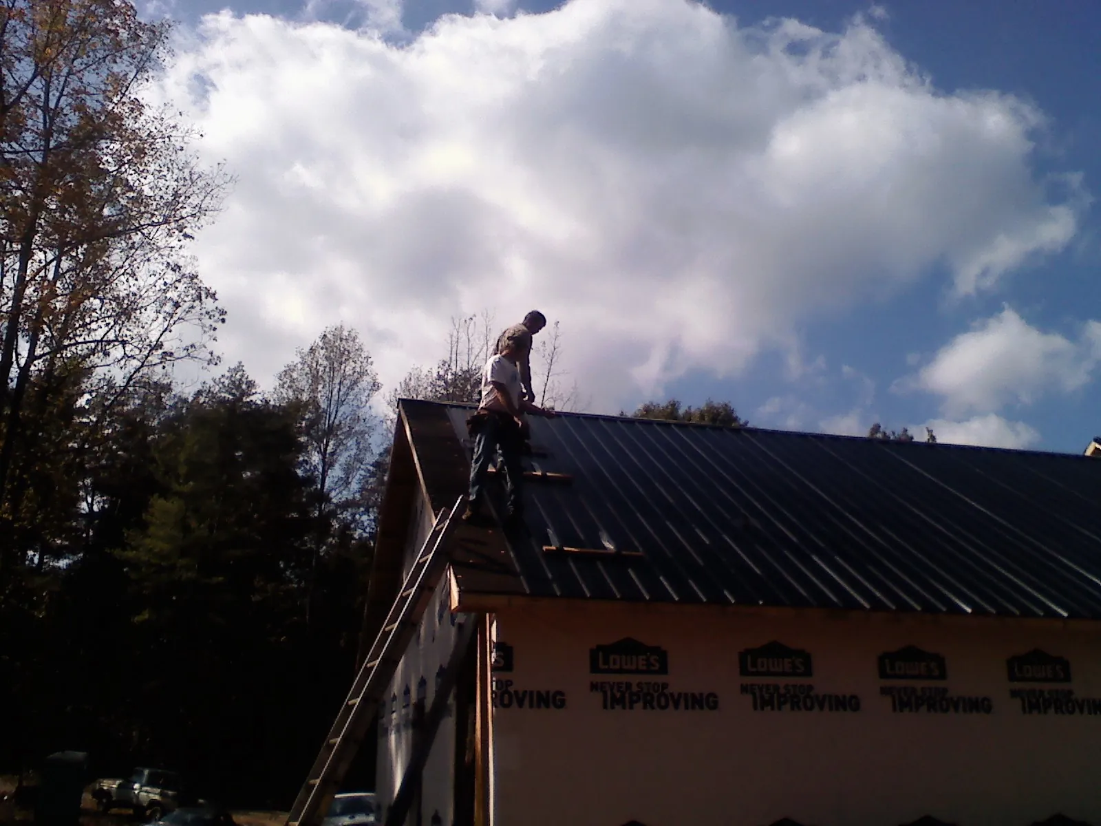 Roofer fastening dark metal panels high against a cloudy sky, from a Roof Inspection job in Penn